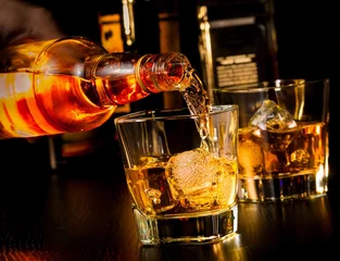 Selbstklebende Fototapete Bar Barkeeper schenkt Whisky vor Whiskyglas und Flaschen ein