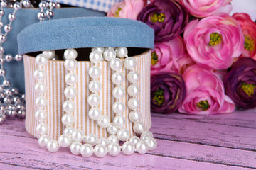 Decorative boxes with beads and flowers on wooden background