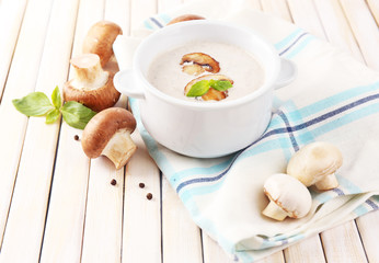 Mushroom soup in white pot, on napkin, on wooden background