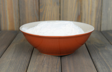 Fototapeta na wymiar Flour in bowl on table on wooden background