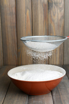 Sifting flour into bowl on table on wooden background