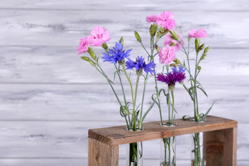 Beautiful summer flowers in vases on grey wooden background