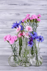 Beautiful summer flowers in vases on grey wooden background