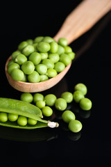 Fresh green peas in wooden spoon isolated on black background
