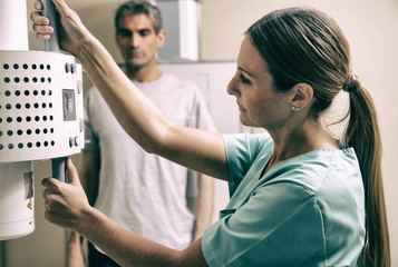 Young female doctor checking x-ray machine before a male patient