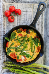 Omelette with asparagus and tomato on frying pan