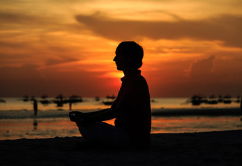 young man doing yoga on sunset beach