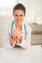 Portrait of happy medical doctor woman showing piggy bank