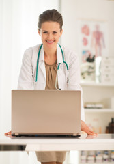 Portrait of happy medical doctor woman with laptop in office