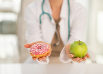 Closeup on doctor woman giving a choice between apple and donut