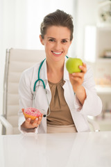 Happy medical doctor woman giving apple instead of donut