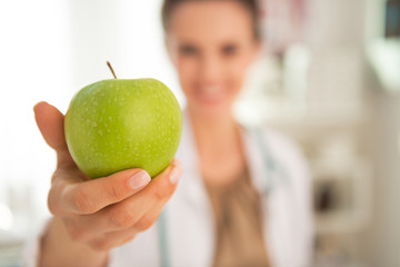 Closeup on happy medical doctor woman giving apple