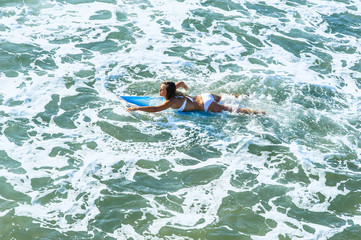 Young attractive surfer paddling through surf on surfboard