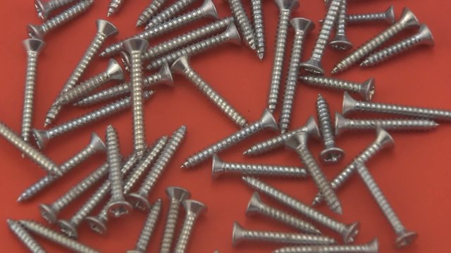 Chrome crosshead screws rotating on a red  background.