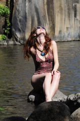 Young girl in a swimsuit sits on a rock and splashes water