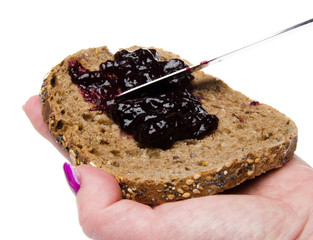 Woman's hand putting blackberry jam on a toast
