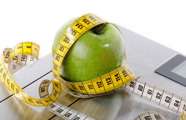 Tape measure around a green apple on a bathroom scales