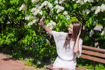 Naklejka premium Young woman take photo on her phone at blossoming lilac garden