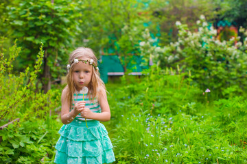 Adorable little girl blowing a dandelion in the garden