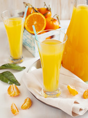 Glass of Citrus juice and fresh oranges and mandarines in rustic
