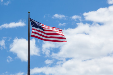 American flag - star and stripes floating over a cloudy blue sky