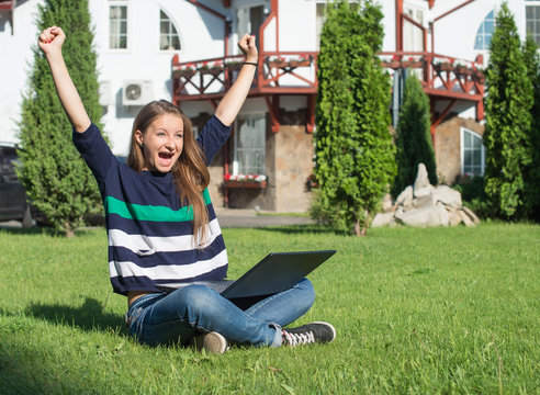 Happy woman student with arms lifted in joy with laptop.