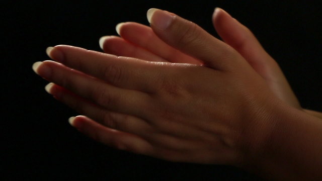 Female hands applaud on a black background, close up