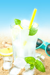 Cold water with lemon and ice on beach background