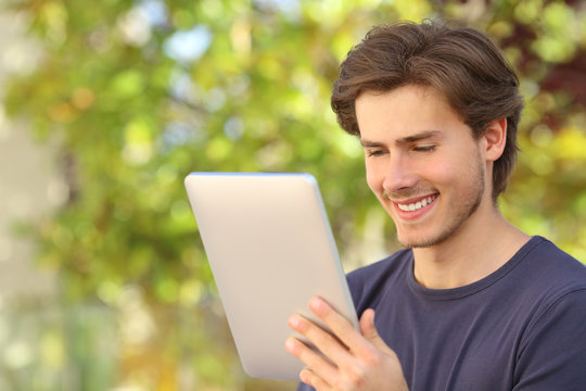 Happy man reading a tablet reader outdoors