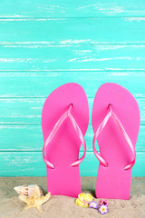 Bright flip-flops on sand, on wooden background