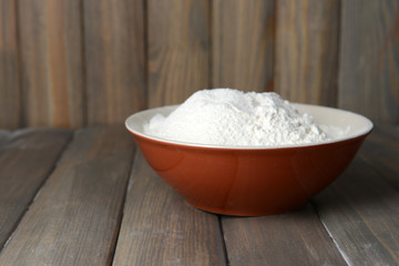 Flour in bowl on table on wooden background