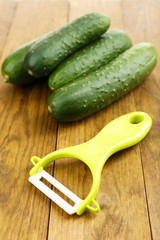Peeler and cucumbers on wooden table