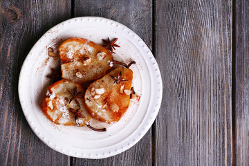 Baked pears with syrup on plate, on color wooden background