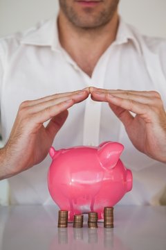 Casual Businessman Sheltering Piggy Bank And Coins