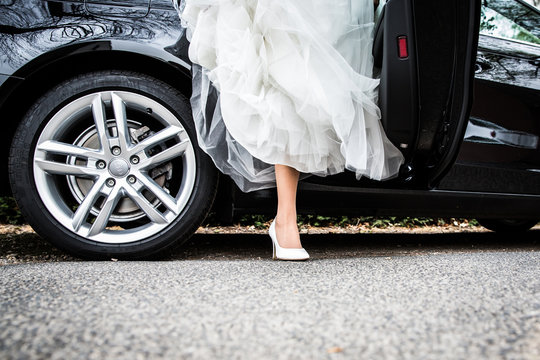 Braut steigt aus dem Brautauto mit wei&szlig;en Schuhen und hohem Absatz
