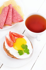 Sandwich with fried egg, tomato slices and tea