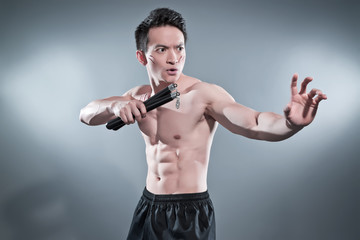 Muscled asian kung fu man in action pose with nunchucks. Blood s