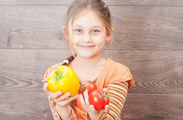 beautiful girl holding a tomato on a wooden background