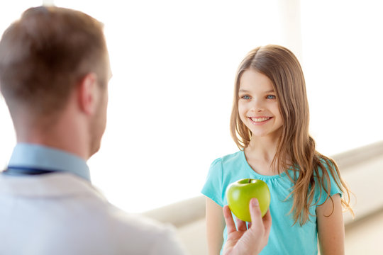 male doctor giving an apple to smiling little girl