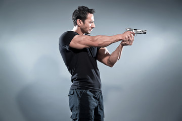 Action hero muscled man shooting with gun. Wearing black t-shirt