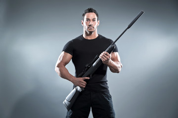 Action hero muscled man holding a rifle. Wearing black t-shirt a
