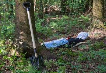 Shovel at the tree and man lying in the forest