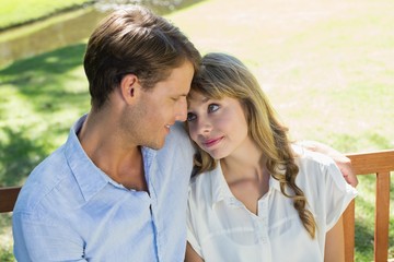 Fototapeta premium Cute couple sitting on park bench together looking at each other