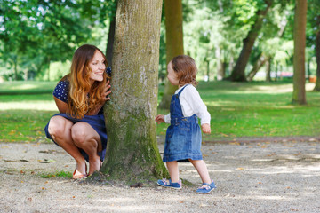 Happy young mother and adorable toddler girl walking through sum