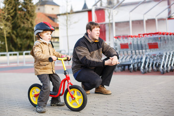 Little toddler boy with bicycle and his father in the city