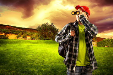 Man traveler looking in binocular standing on green valley