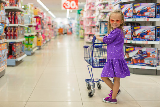 Little fashion girl with trolley in a large shopping center