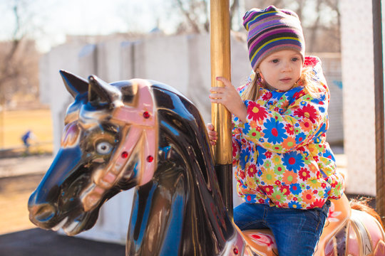 Little adorable girl on carousel at sunny day outdoor