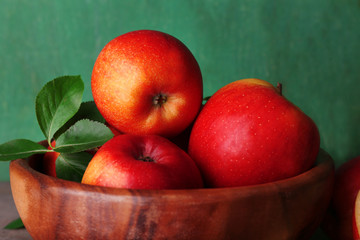 Ripe sweet apples with leaves in bowl on wooden background