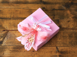 Pink gift with bow and flower on wooden table close-up